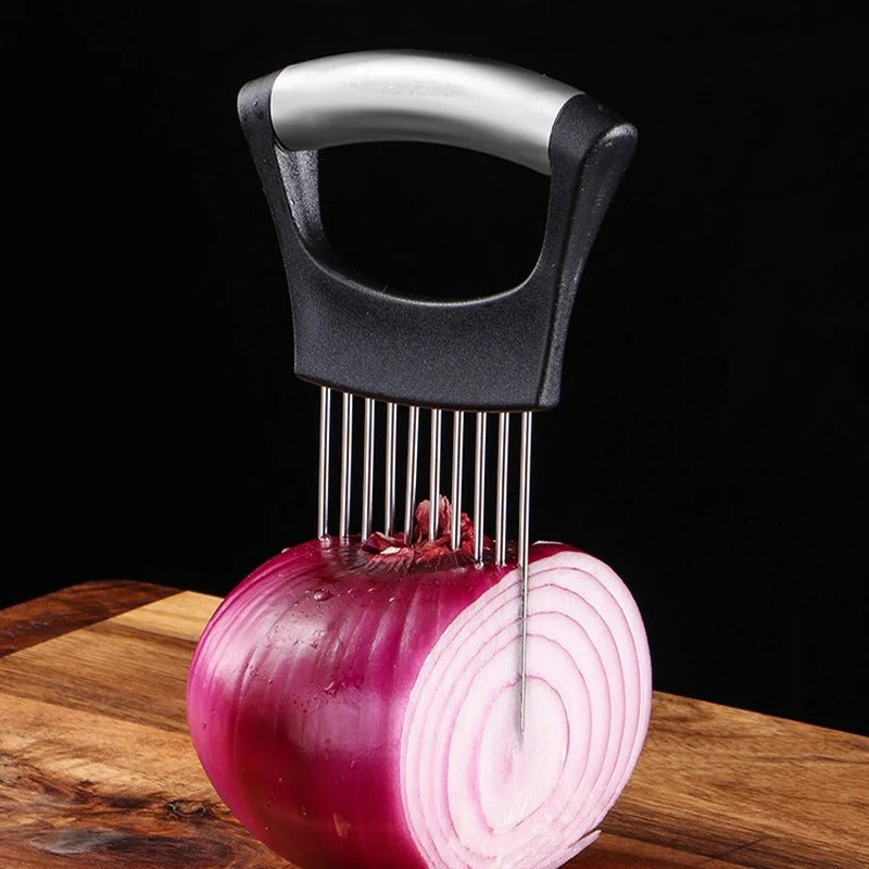 The Stainless Steel Onion & Tomato Slicer Holder, a kitchen gadget with parallel prongs, is inserted into a halved red onion on a wooden cutting board to guide precise knife cuts. The background is black.
