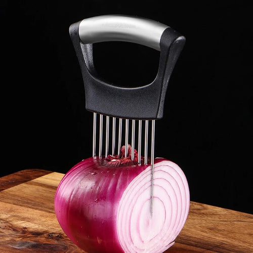 The Stainless Steel Onion & Tomato Slicer Holder, a kitchen gadget with parallel prongs, is inserted into a halved red onion on a wooden cutting board to guide precise knife cuts. The background is black.