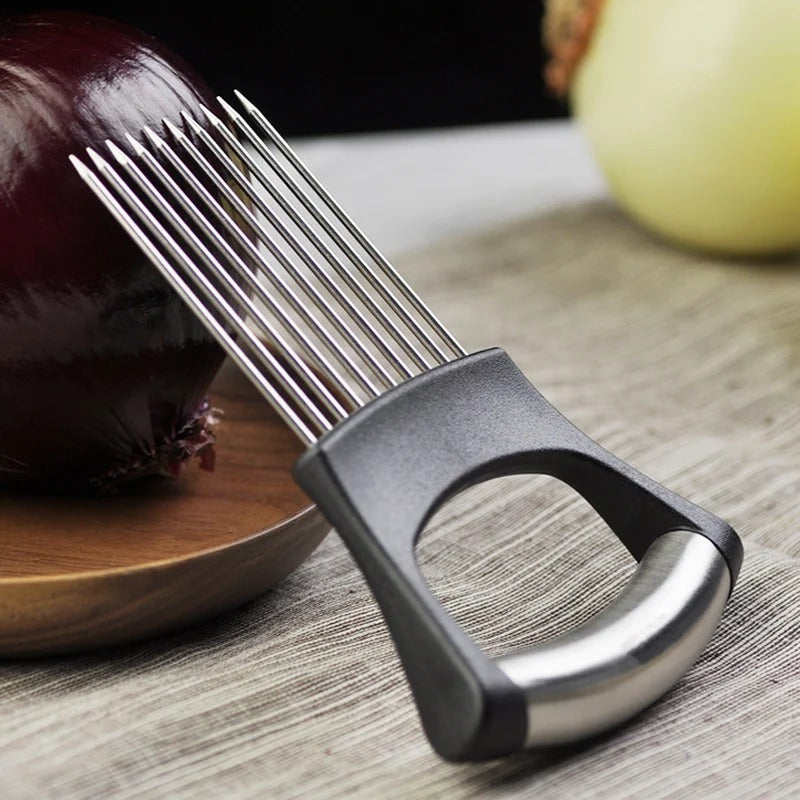 The Stainless Steel Onion & Tomato Slicer Holder, a vegetable cutting fork with multiple prongs and black handle, sits beside a red onion on a wooden plate—a safe kitchen gadget for easy food slicing.