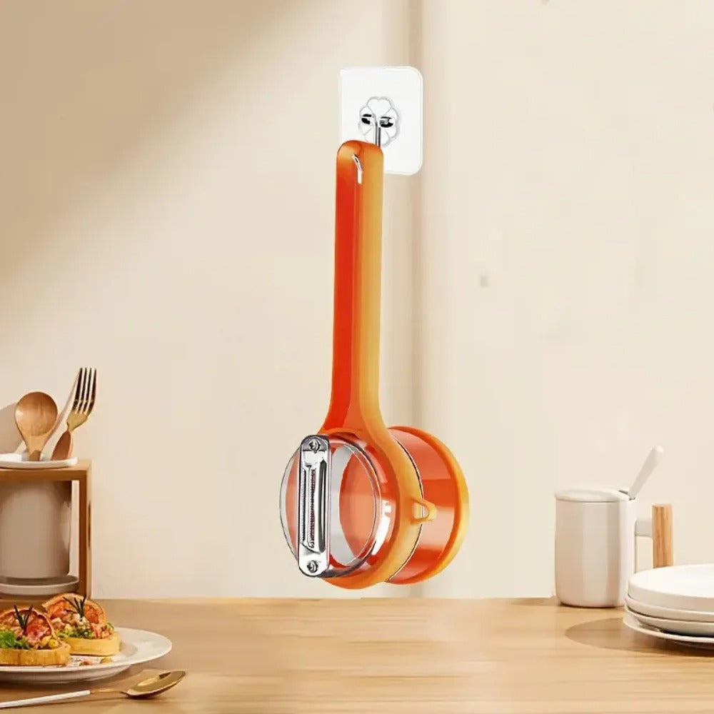 A Double-Sided Stainless Steel Peeler with Storage Box hangs vertically on a wall hook in the kitchen, with a set dining table and utensils visible in the background.
